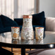 Copper water bottle with floral golden pattern and two printed drinking tumblers in curved design by Indian Art Villa.