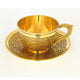 Polished brass tea cup with circular base and embossed body resting on round saucer with matching floral pattern detailing