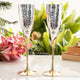 Two silver and gold champagne flutes on a table with flowers and a box in the background.