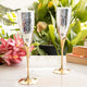 Two silver and gold champagne flutes on a white surface with pink flowers and greenery in the background.